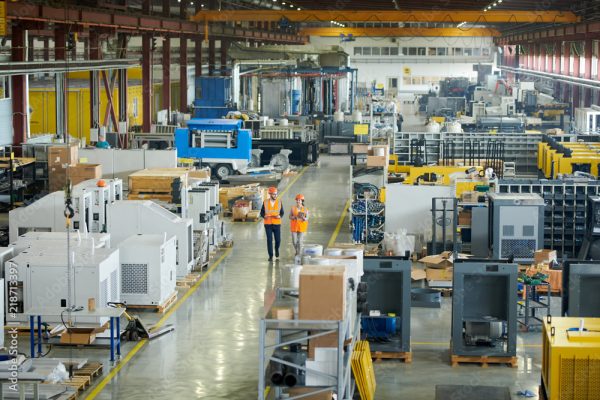 High angle full length portrait of bearded businessman wearing hardhat walking across production workshop accompanied by female factory employee, copy space